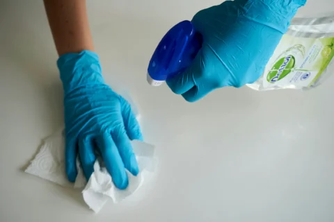 Two gloved hands wiping a surface with cleaning tools.