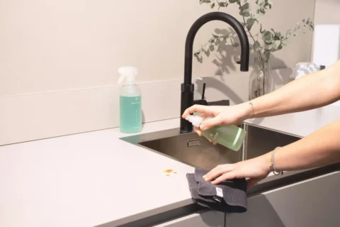 Cleaning a sink with a spray bottle and microfiber cloth.