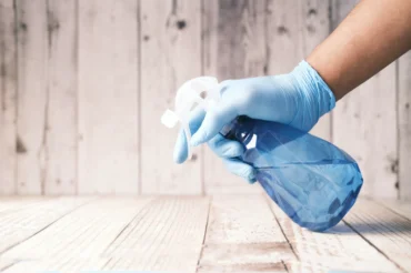 Gloved hand spraying a countertop for thorough cleaning.