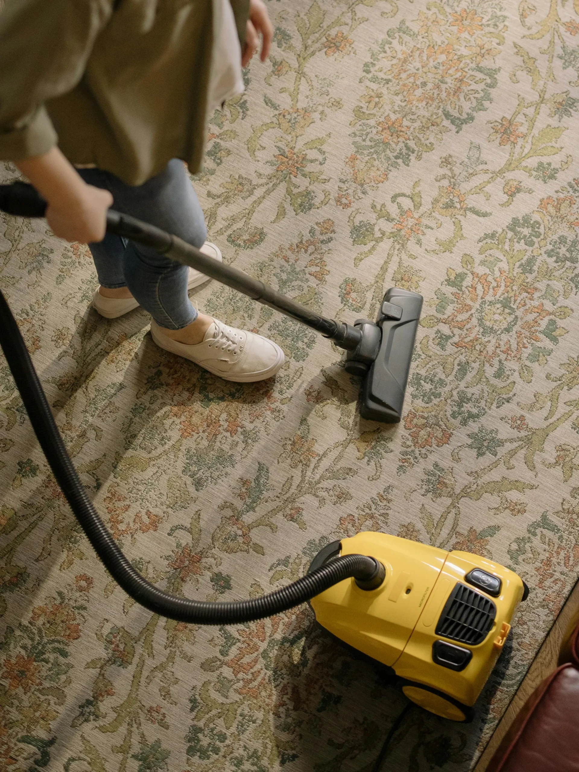 Woman in green button-down vacuuming a carpeted floor for deep cleaning.