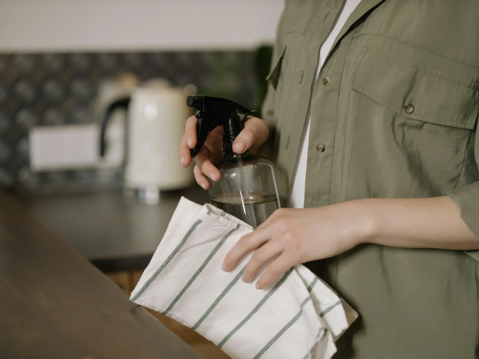 Woman in green button-down holding cleaning supplies, symbolizing professional cleaning services.