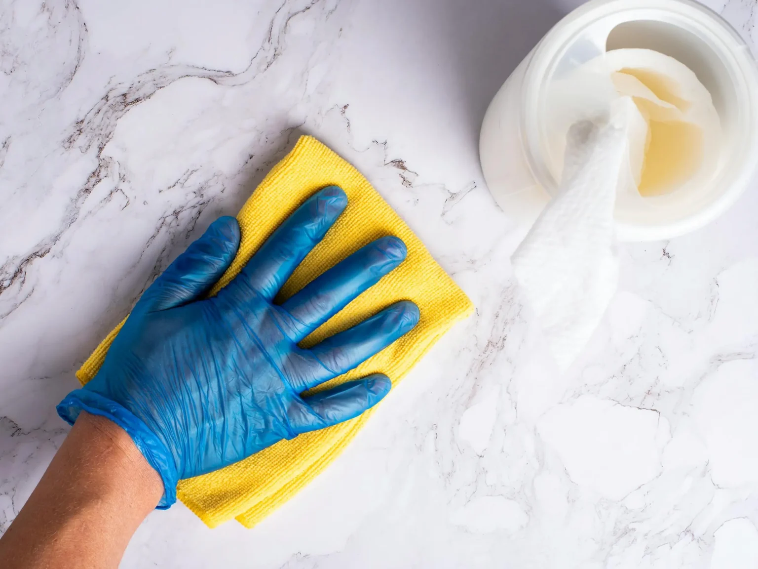 Gloved hand wiping a quartz countertop with a yellow microfiber cloth.