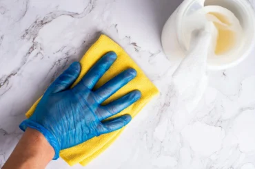 Gloved hand wiping a quartz countertop with a yellow microfiber cloth.