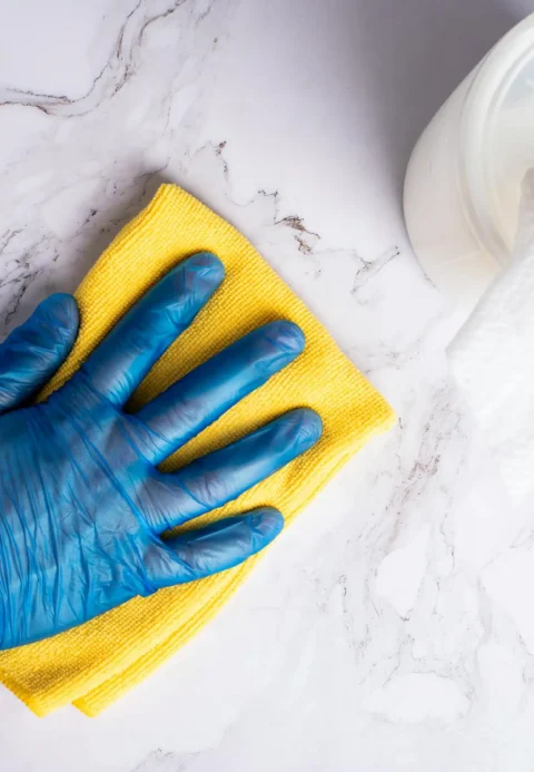 Gloved hand wiping a quartz countertop with a yellow microfiber cloth.